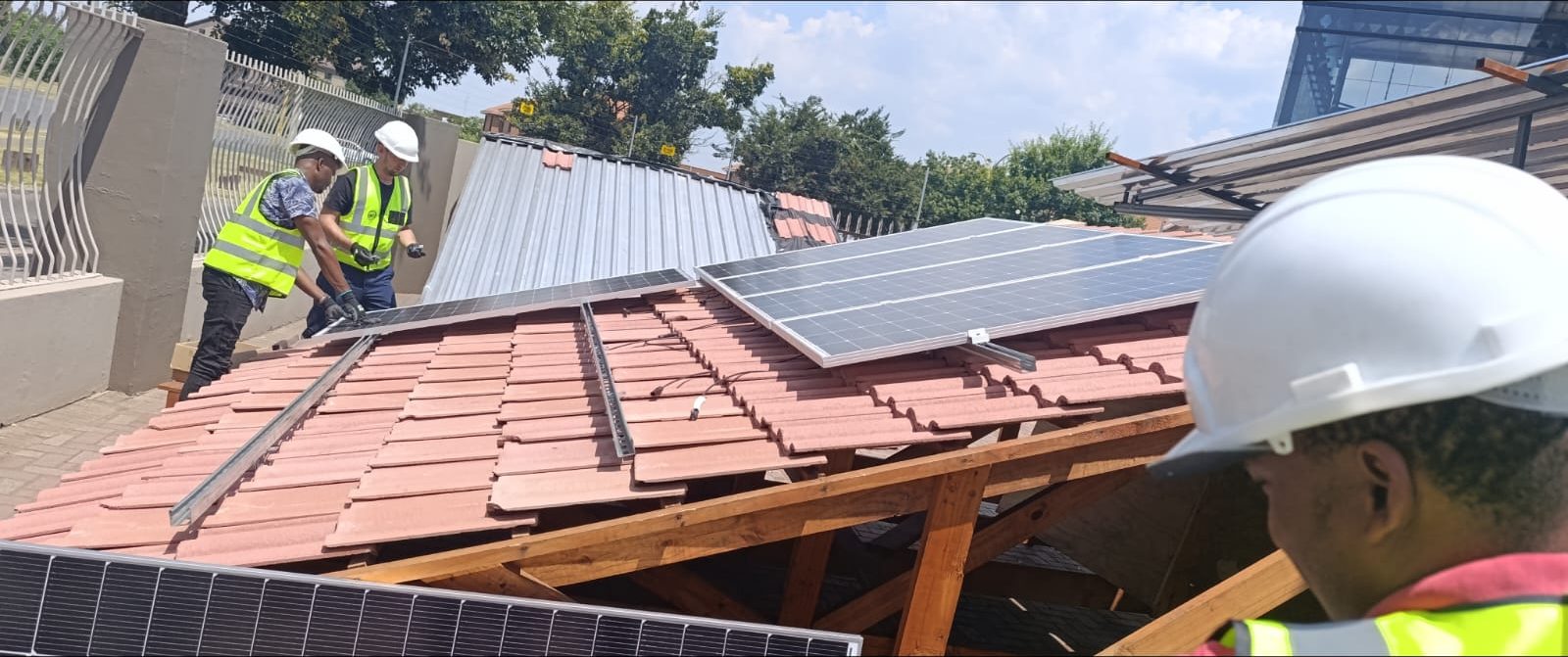 Trainees fitting mounting rails and PV panels on a tiled training roof
